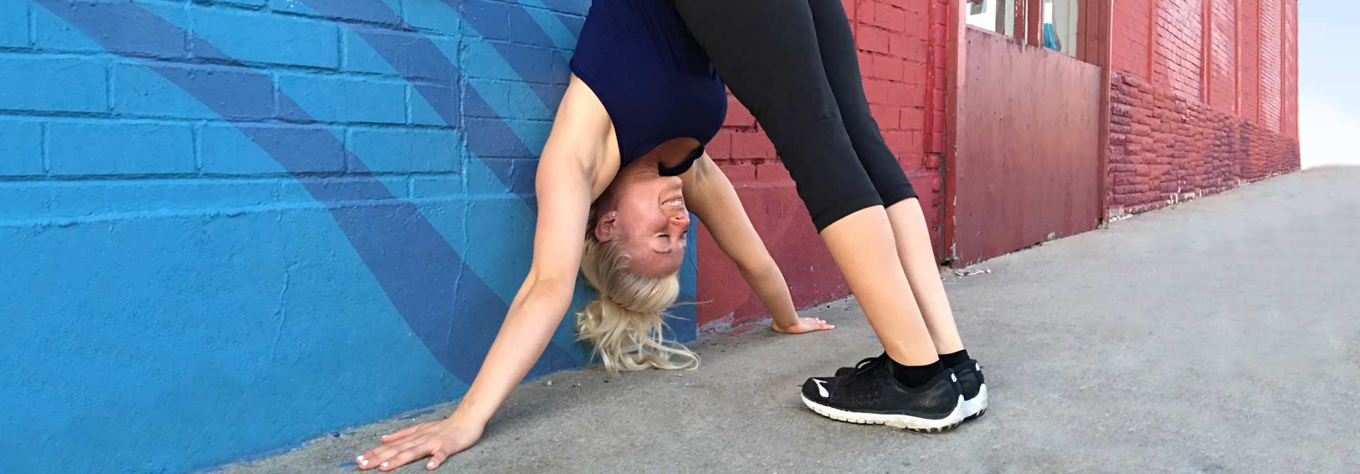 Atleta de GymnasticBodies demuestra un estiramiento de cuerpo entero contra la pared.